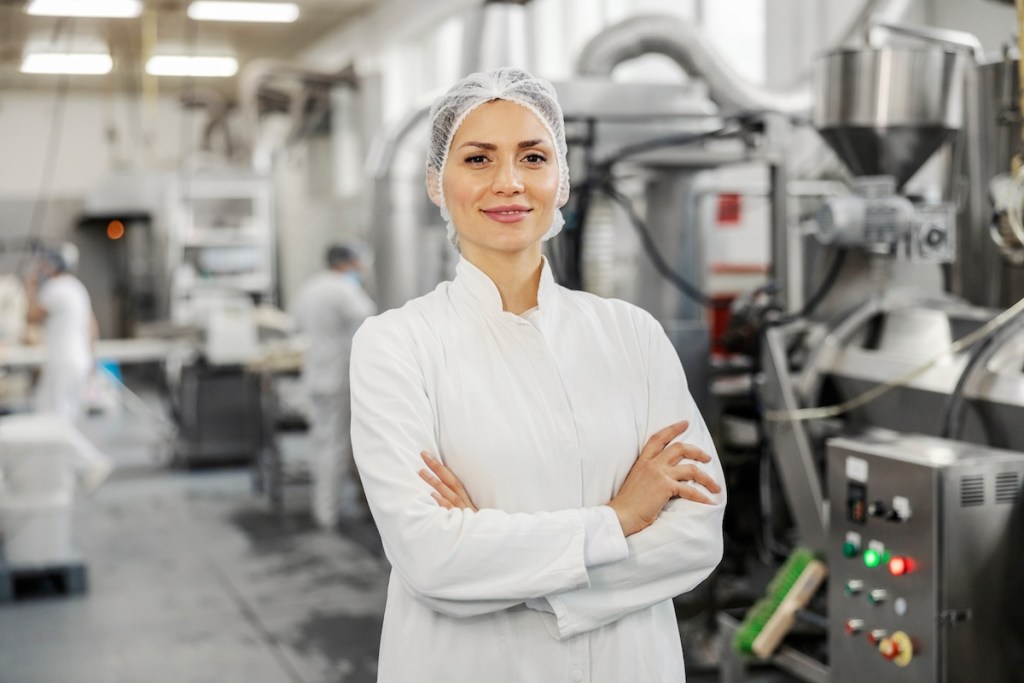 portrait of a successful food factory manager in sterile uniform with arms crossed smiling at the camera.